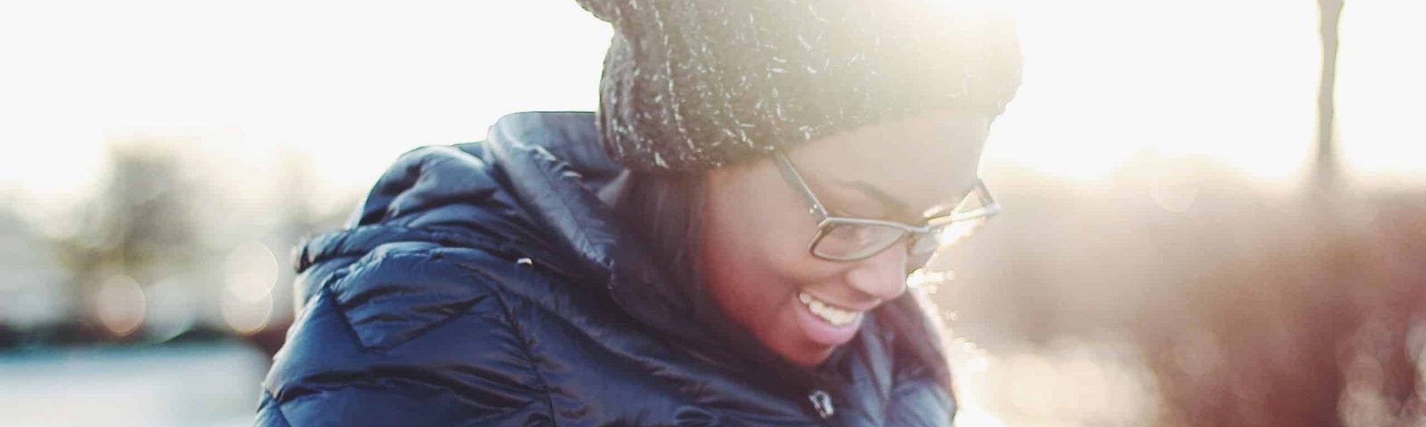 Dark skinned woman walking in cold weather checking her smartphone, smiling and scrolling