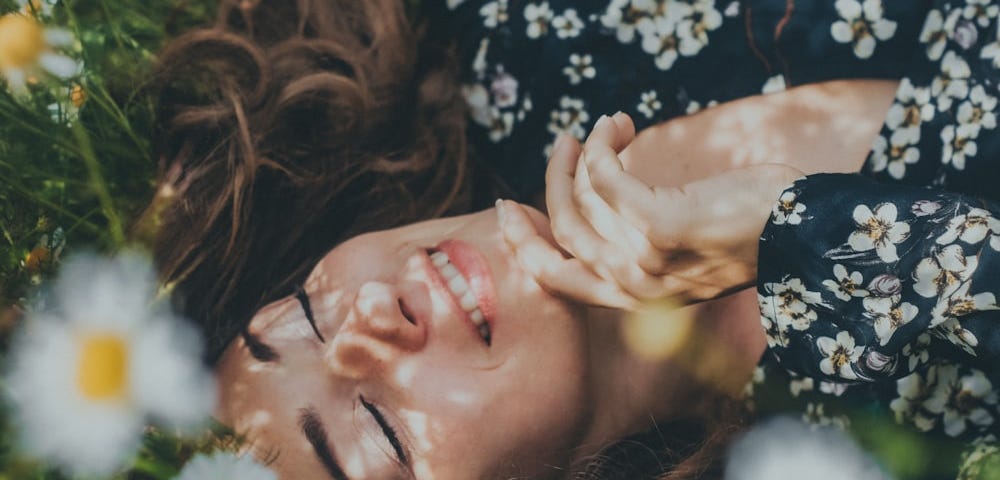 Woman lying on the grass with her eyes closed and smiling.