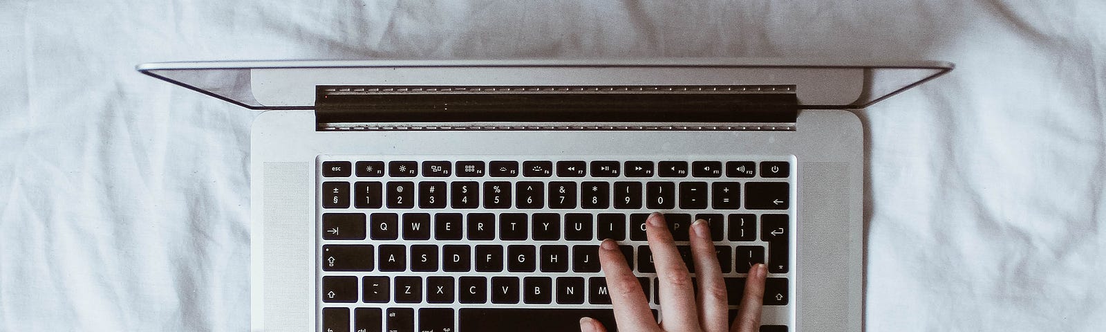 Hands typing on a laptop on a white bedspread