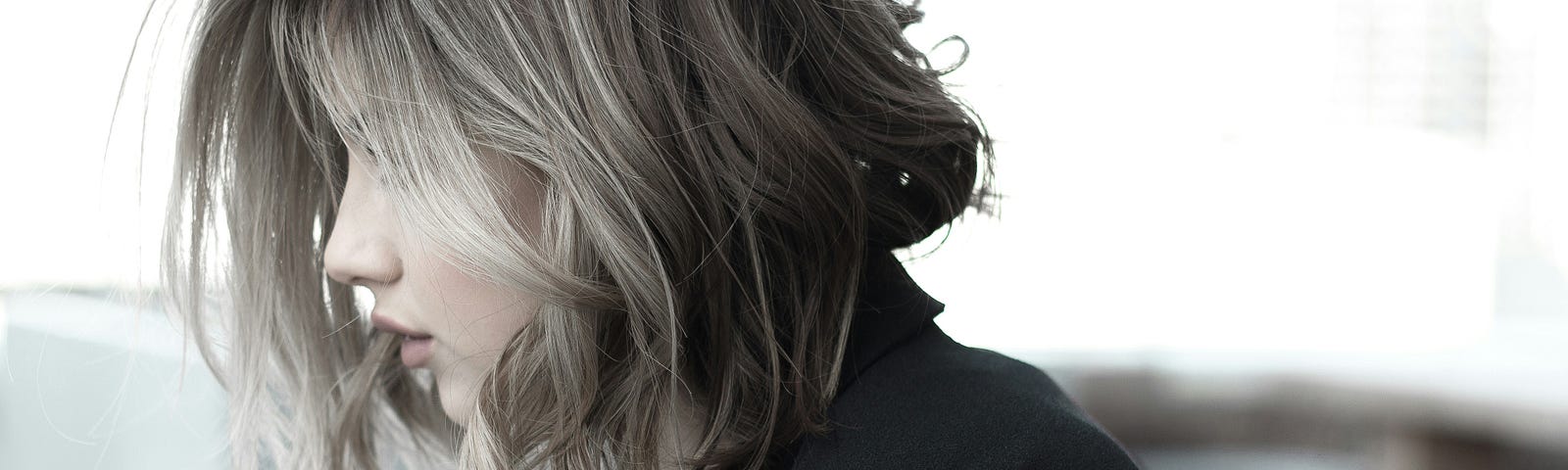 Photo from Upsplash of a seated woman in a black top with shoulder length hair that has gray streaks. Her hair is falling forward and covers much of her profile, only her nose and mouth can be seen.