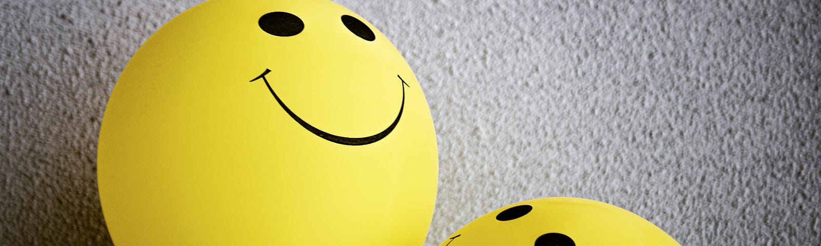Three bright yellow balloons with smiley faces on them.