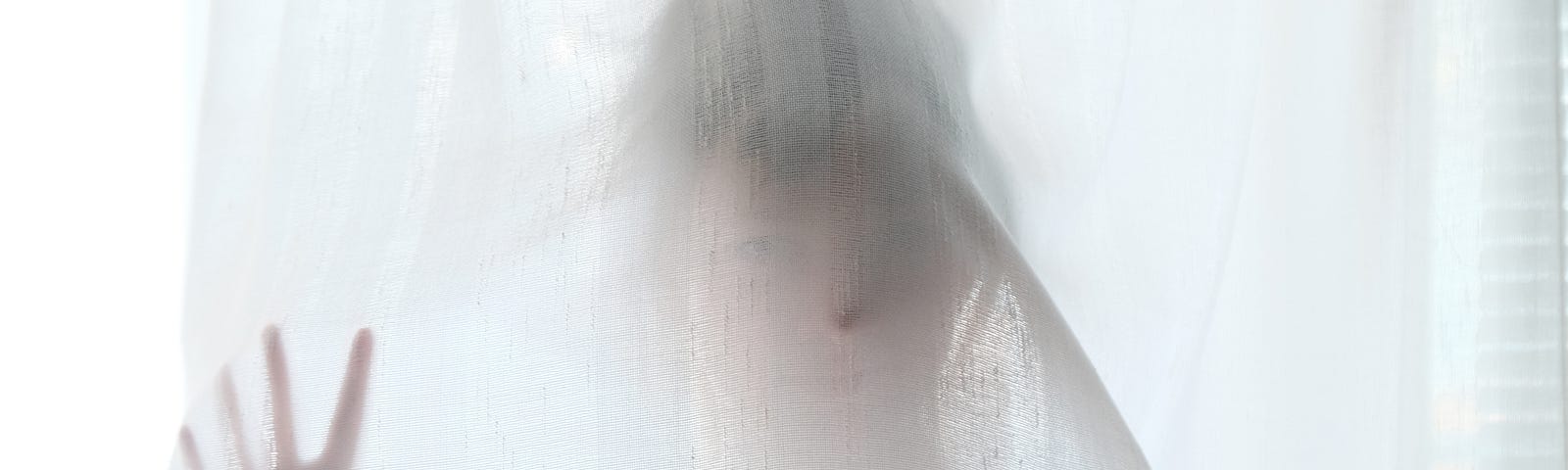 A woman behind a curtain with hand pressing against it, appearing as if a ghost.