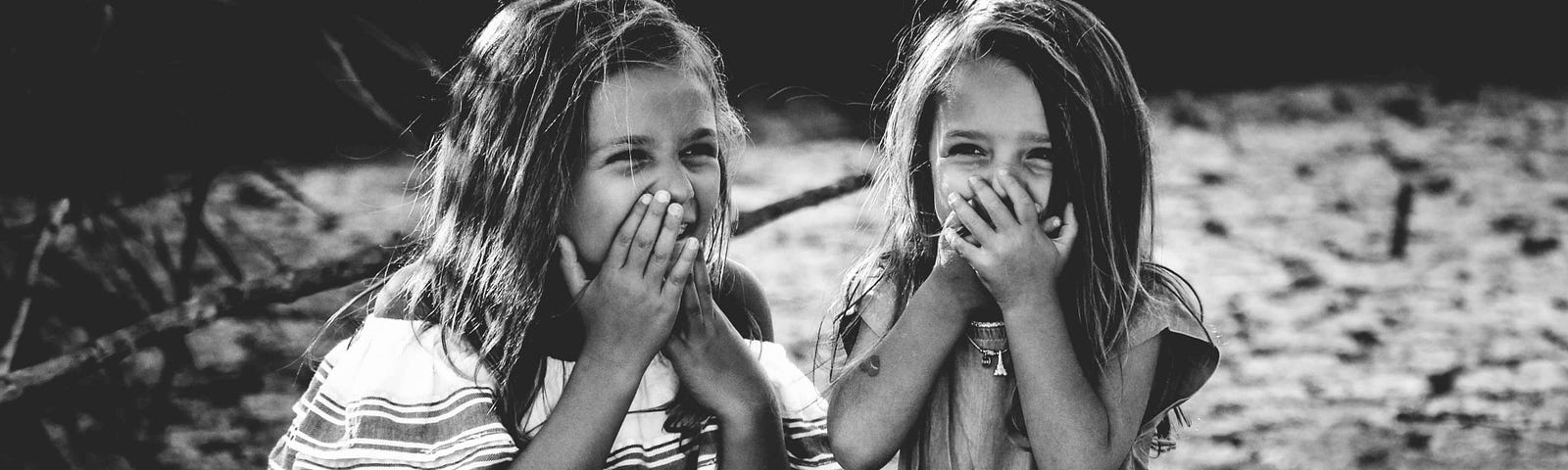 Two little girls cupping their mouths while giggling.