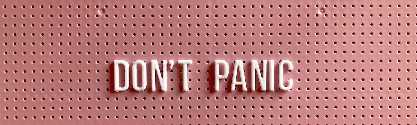Pink pinboard with the words “Don’t Panic” pinned to it