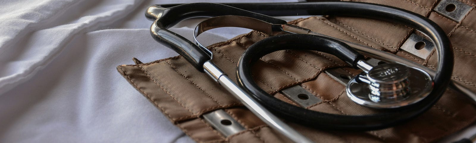 A sphygmomanometer and stethoscope lying on a white bedsheet