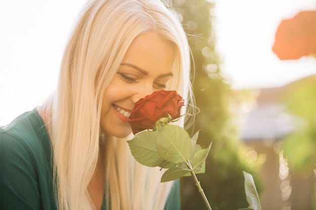 Smiling beautiful young woman smelling red rose