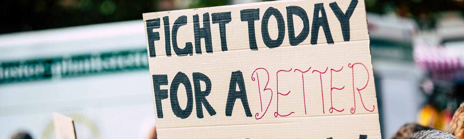 A cardboard sign at a climate change protest. Held above the heads of the crowd, it proclaims; “Fight Today For a Better Tomorrow”.