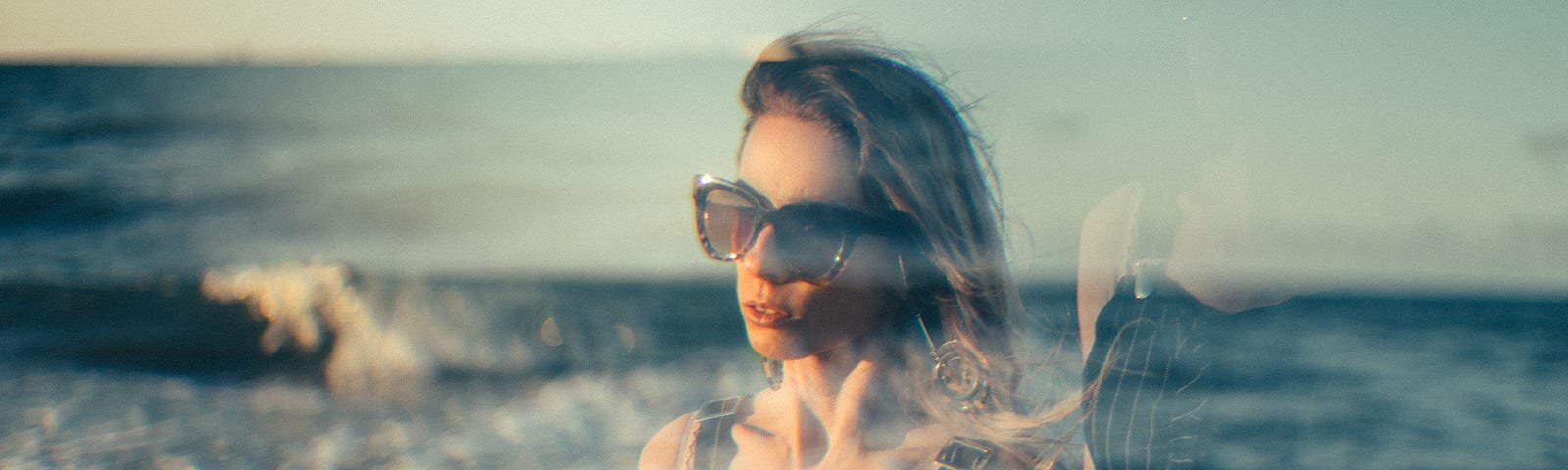 Woman wearing sunglasses with ocean waves in background of pic.