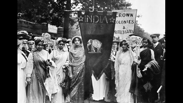 Image description: A black and white photo of Indian suffragettes at the 1911 Coronation Procession holding a triangular flag with the word India and an elephant beneath.
