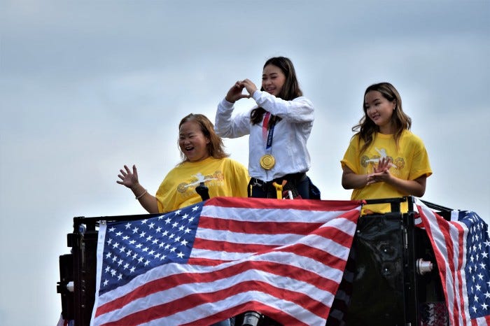 Suni Lee, her mom, and her sister on top of a fire truck and waving to a crowd.