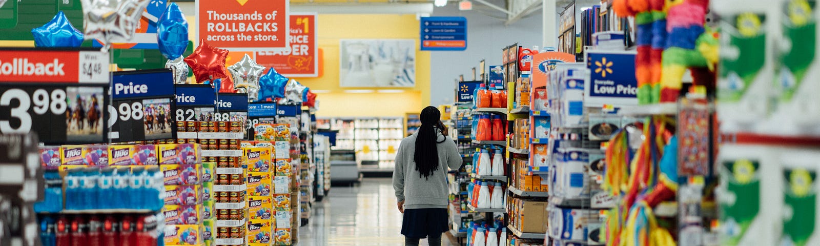 A woman walking down a grocery store aisle and talking on the phone.