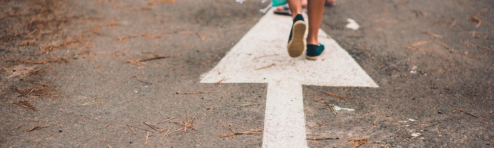 A picture of an arrow drawn on concrete with a person walking away from the camera in the direction the arrow is drawn.