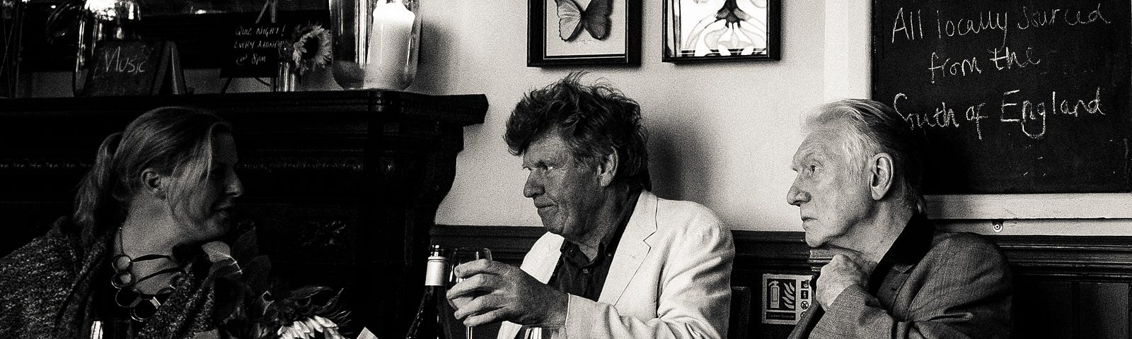 A black and white pic of three people sitting at a table and having a drink