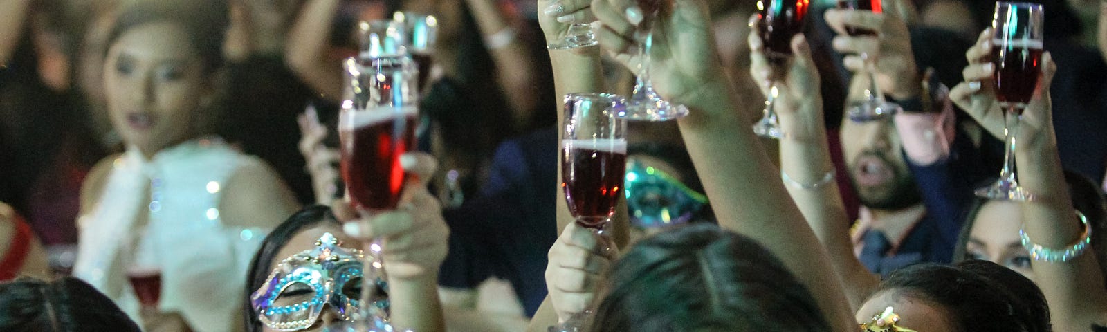 Women raise wine glasses and cheer, some masked.