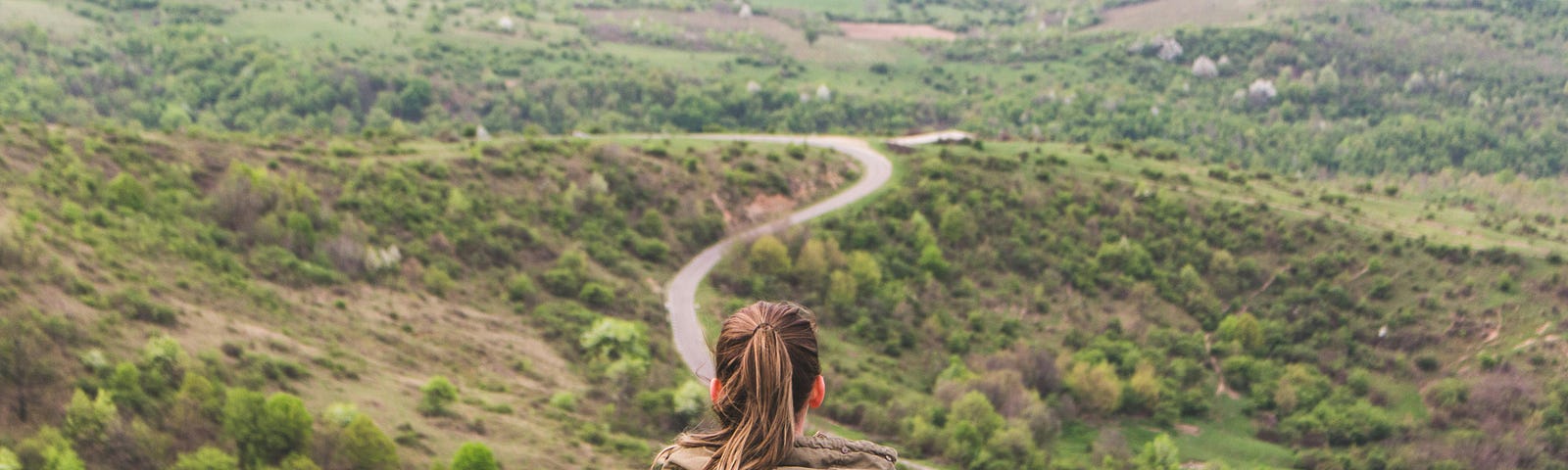 Woman sitting on a hill looking over a long winding road.