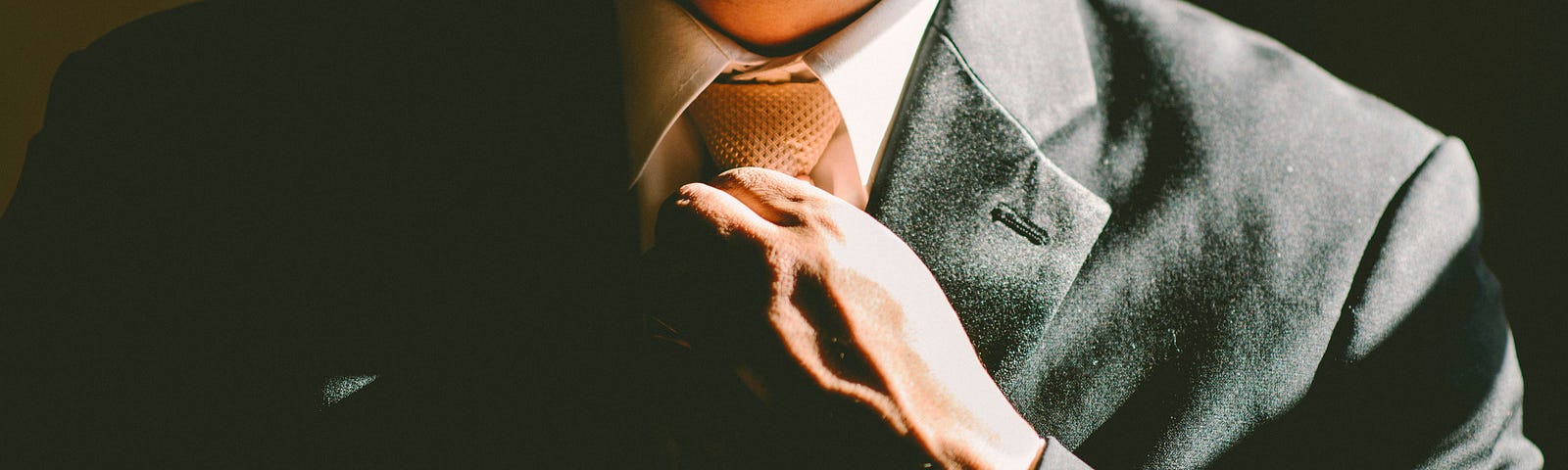 A close up on someone’s suit jacket as they tighten their tie