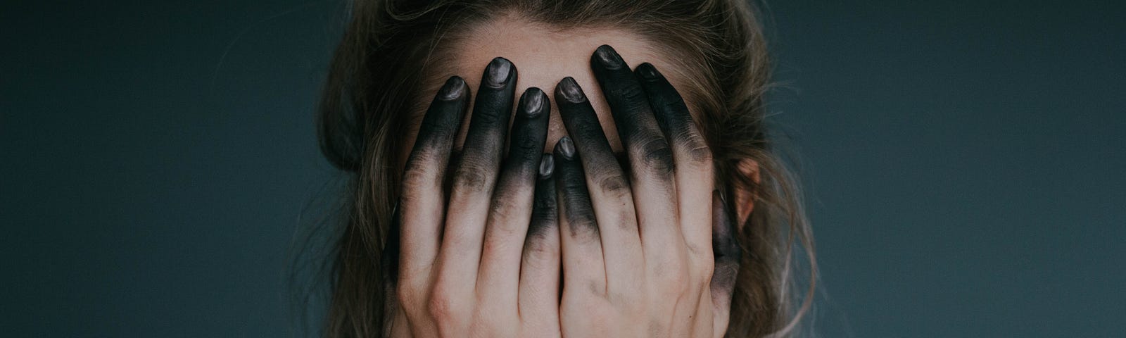 Image of a woman covering her face with black-stained fingertips.