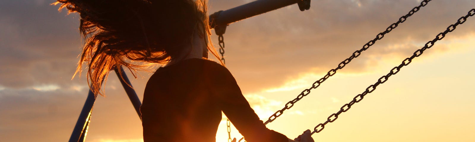 Girl on swing at sunset with her hair flying behind her.