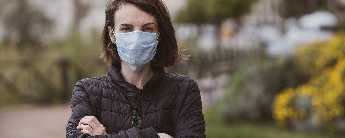 woman in black puffy jacket standing outside with her arms folded in front of her wearing medical mask