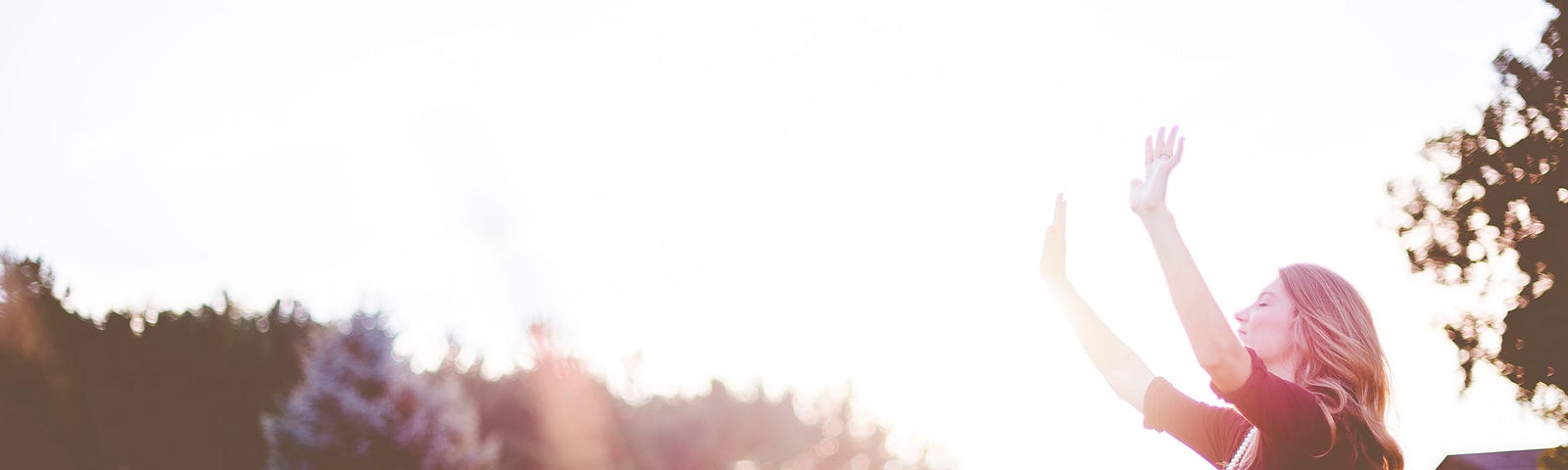 A young adult woman raises her hands in praise out in nature.