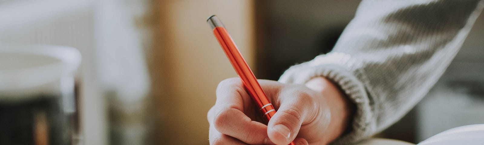 A person sits at a table writing with an orange coloured pen in a thick notebook.