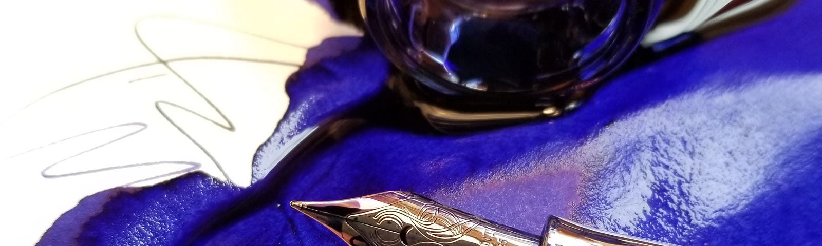 A fountain pen nib, an overturned ink pot and a puddle of blue ink.