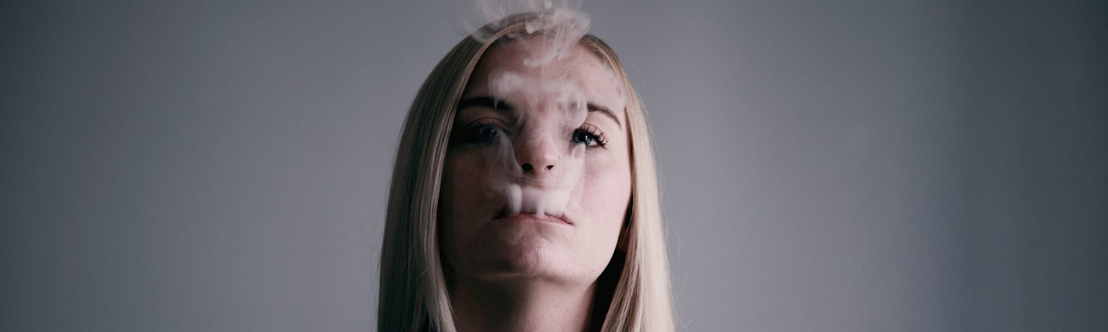 A girl with blonde hair with smoke coming out of her mouth