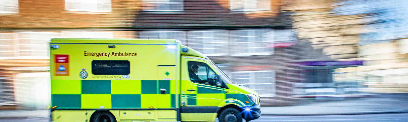 NHS yellow and blue coloured emergency ambulance driving quickly down a road.