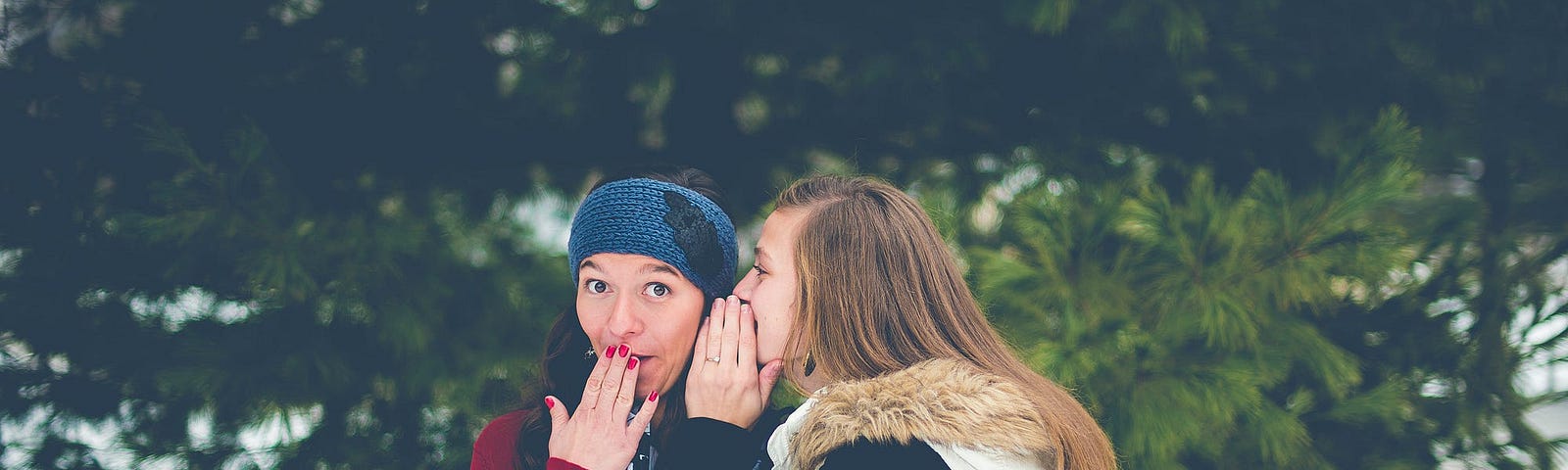 A teenage girl whispers into another girl’s ear