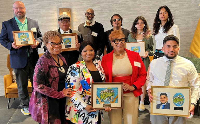 A group of people posing for a photo and holding up framed versions of their work.