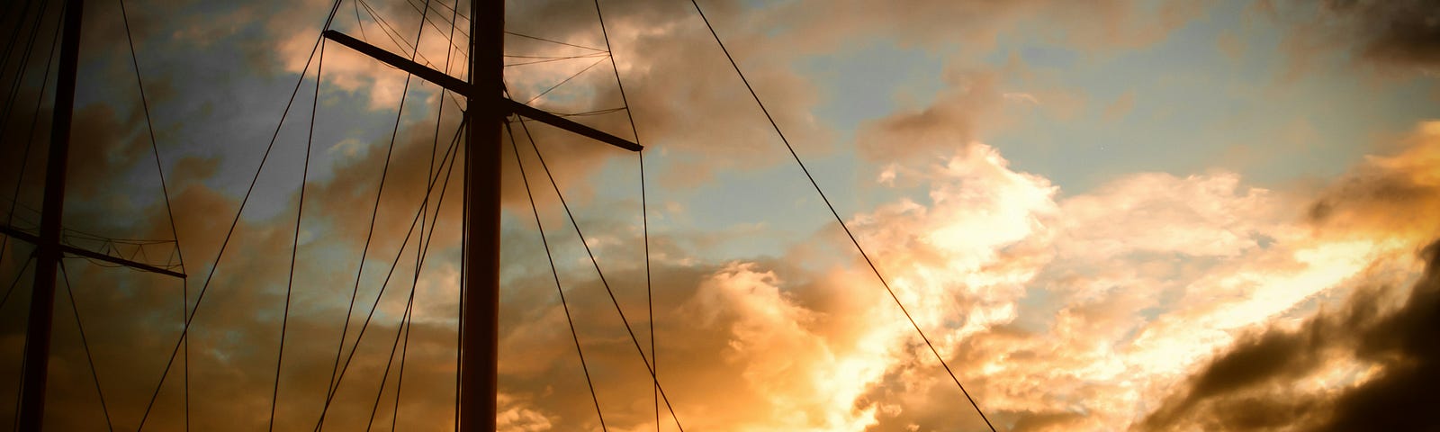 The masts of a ship after a storm. The amber clouds are giving way to a blue sky.