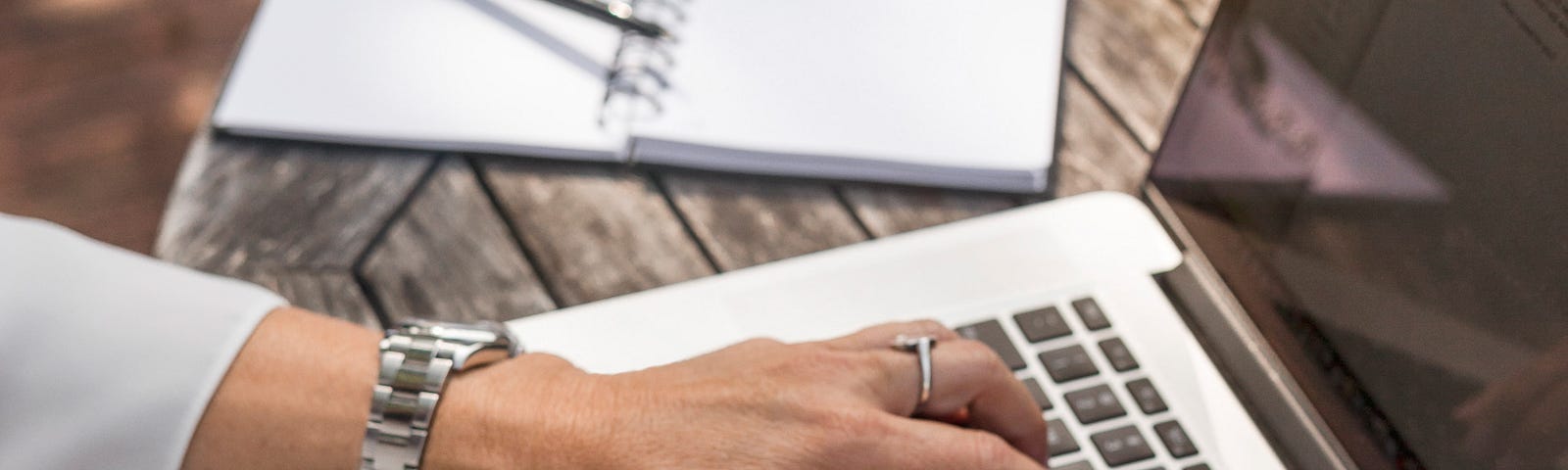 Bejeweled Hands on keyboard on wood- worn dusk with opened notebook at the left corner of her rustic desk.