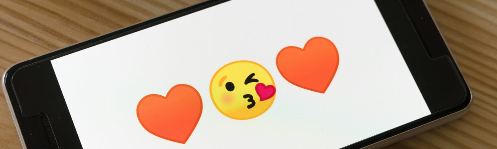 Phone screen showing emojis: heart, kissing face, heart.