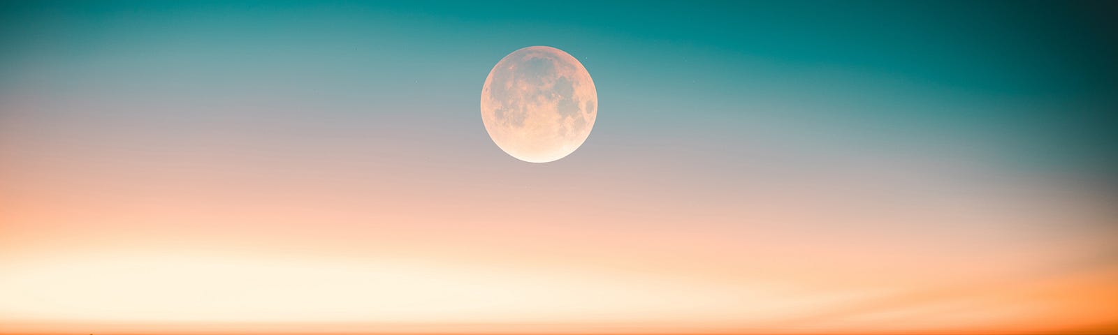 Photo of a moon over ocean, seen above shades of white, pink-peach and blues in the sky, mountains in foreground.