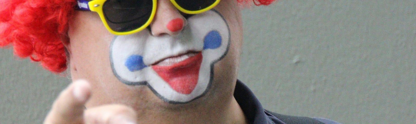 A photo of a clown in a red wig with yellow sunglasses, wearing a police badge