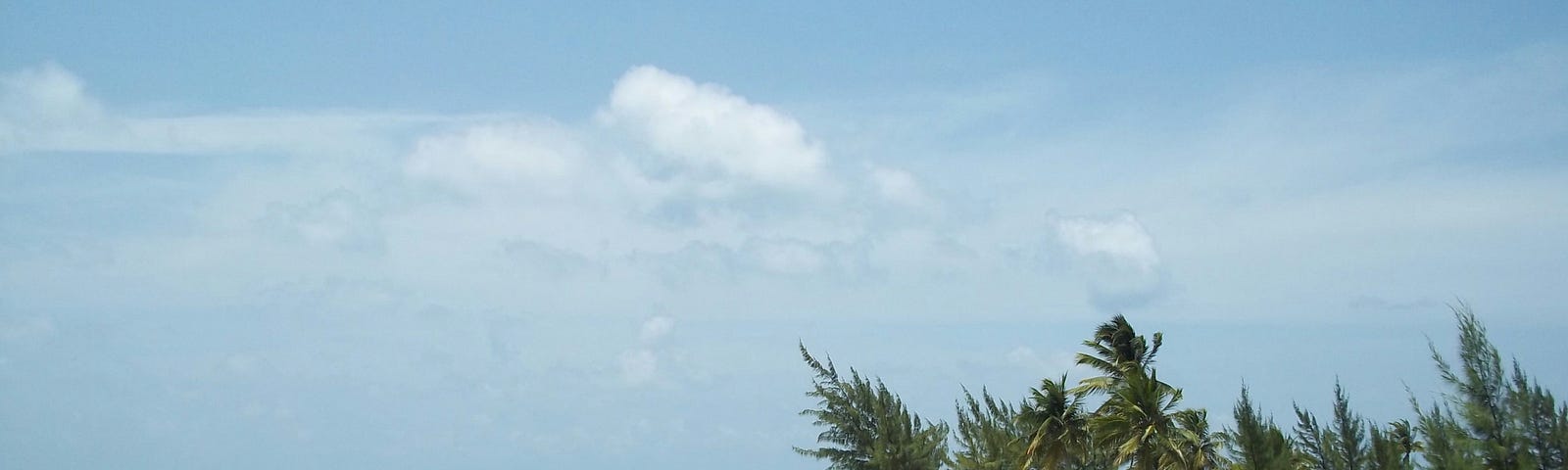 An emerald sea with a white sand beach in the distance with a hazy blue sky.