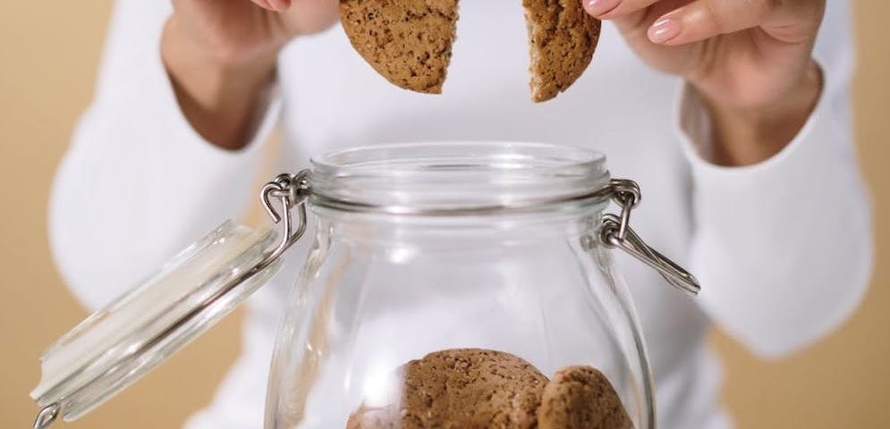 Close-up of woman taking a cookie out of a cookie jar.