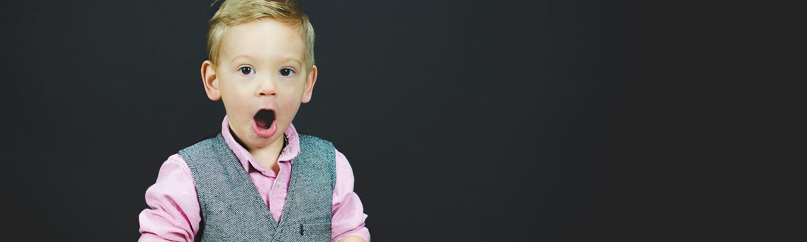 Kid in suit vest holding a book with a surprised expression.