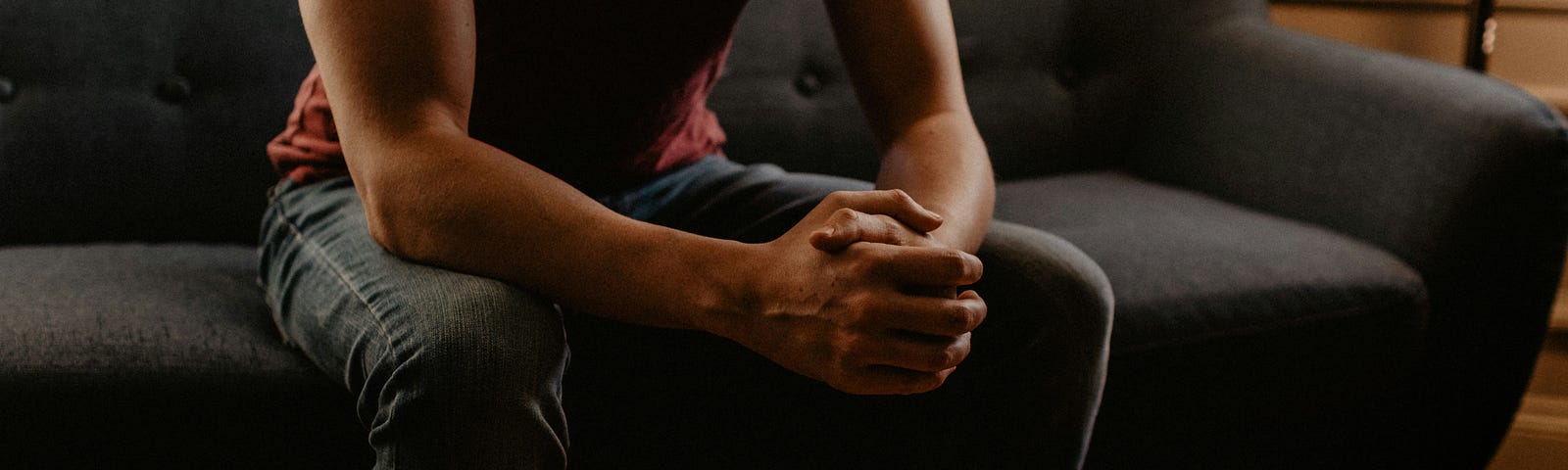 Man sitting on the edge of a sofa, hands clasped.