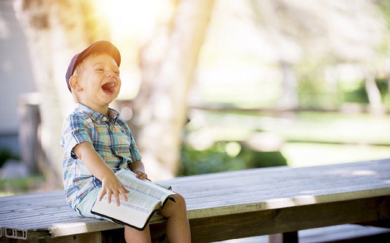 A little child sitting on a bench, laughing, holding in his hands an open book