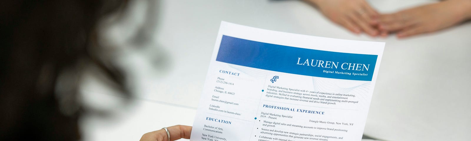 A photo of someone sitting at a table revieiwng a resume with the name “Lauren Chen” at the top.