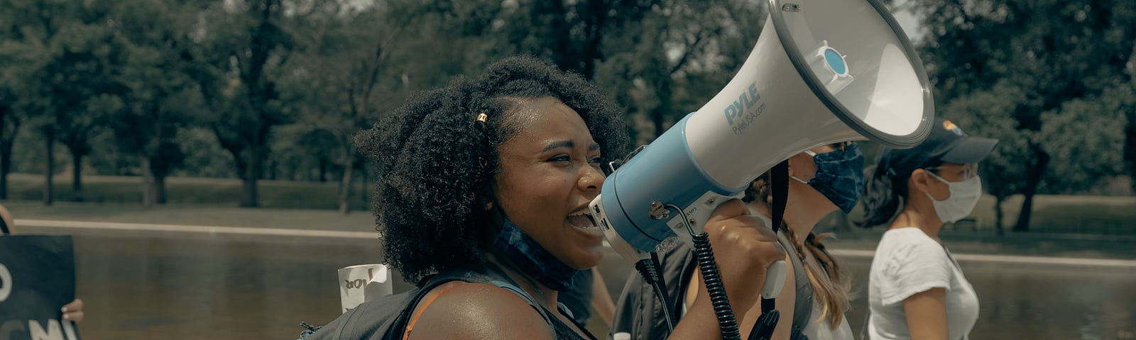 Black woman speaking into a bull horn and walking beside other women.