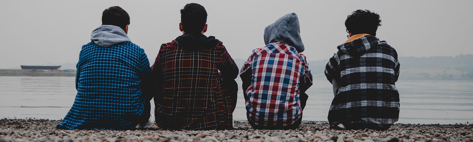 Four boys sitting and staring at the sea. We see their backs. y website: www.elladejong.com/en