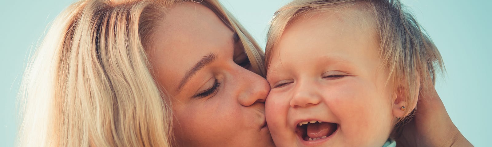 Woman with blonde hair her kissing a small baby on the cheek