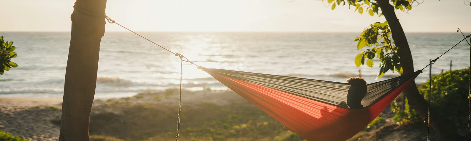 Person in silhouette sitting in a red hammock overlooking the ocean