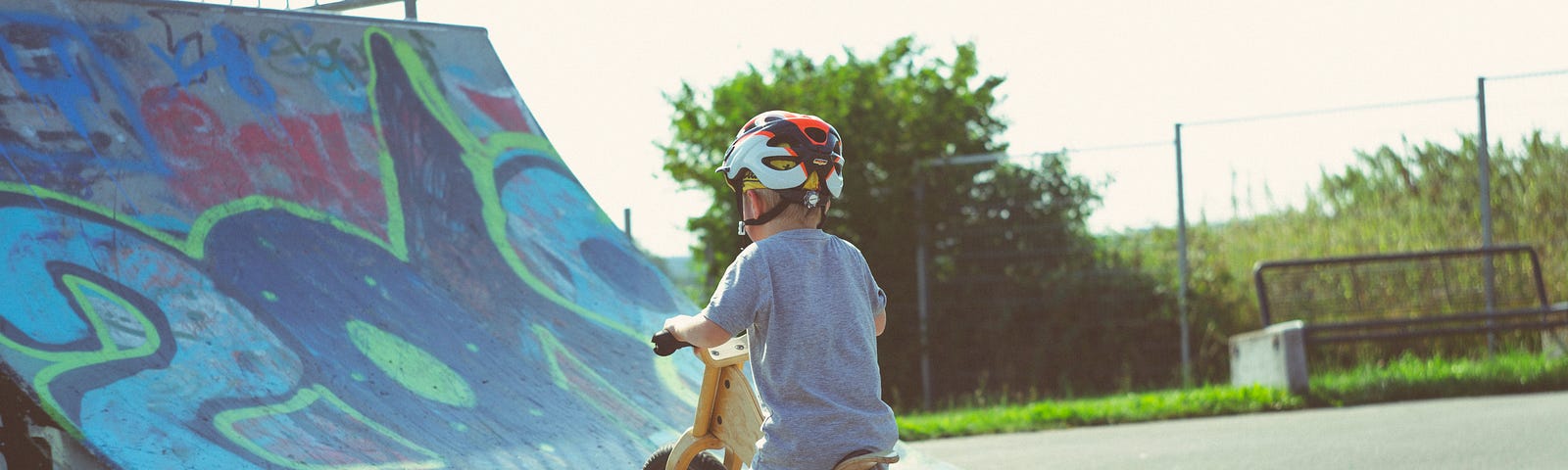 A little boy considering whether he should ride up a ramp on his bike.