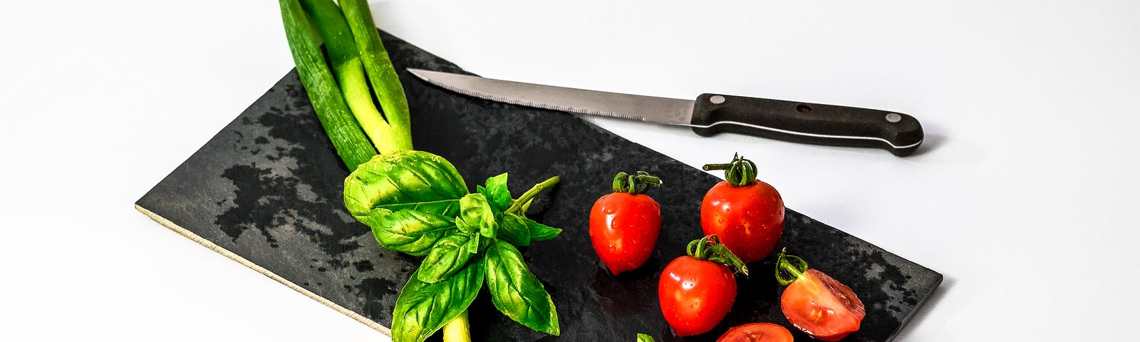 Black long, rectangular flat board with tomatoes and vegetables on it.