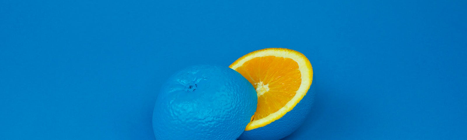 An orange, sliced in half, painted blue on a blue background