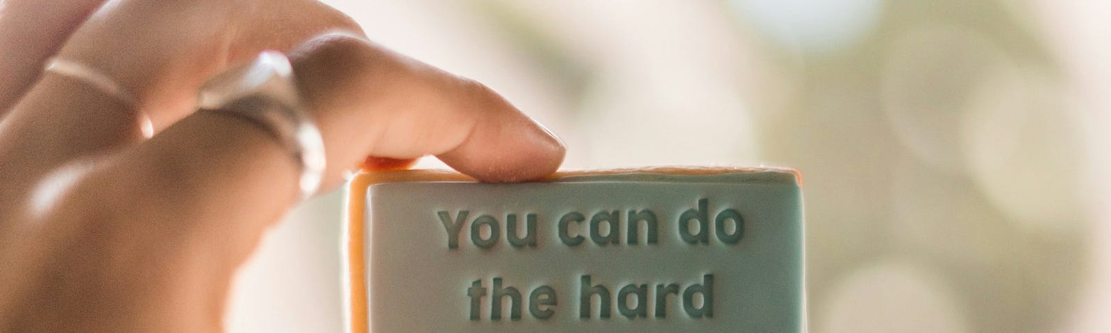 woman’s hand holding up a sign that says “ you can do the hard things.”