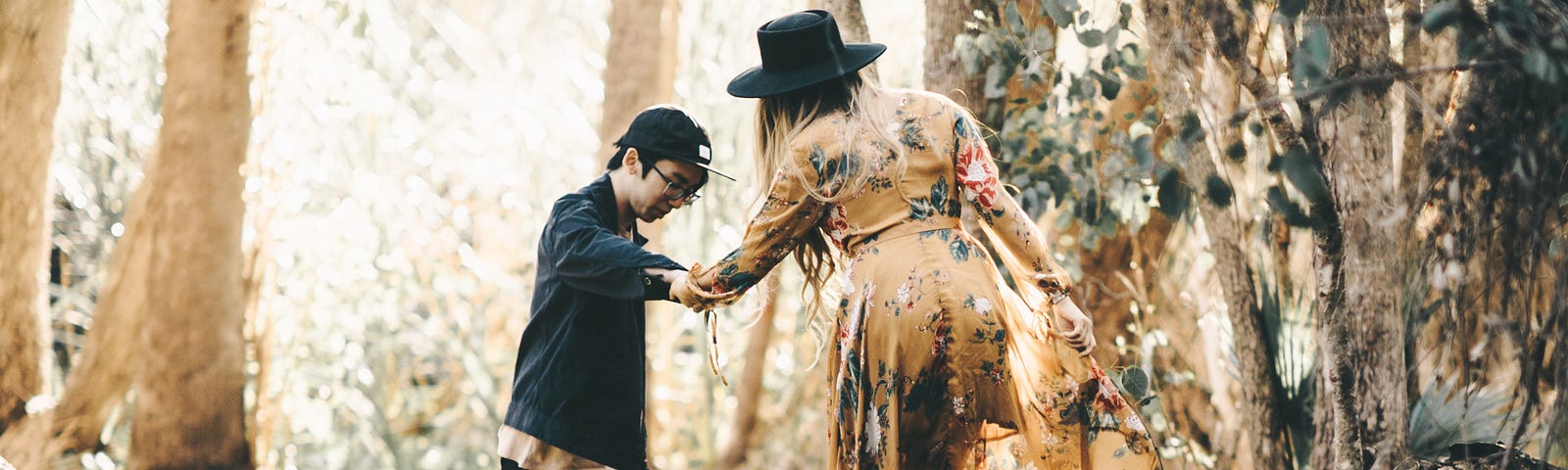 Man holding a woman’s hand as they walk through the forest together